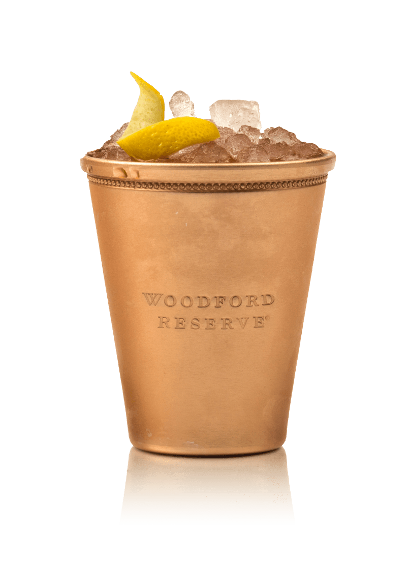 Mosiężna szklanka z logo Woodford Reserve wypełniona drinkiem, lodem i garniszem